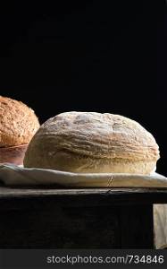 baked round white wheat bread on a textile towel, wooden old table, black background. Homemade food.