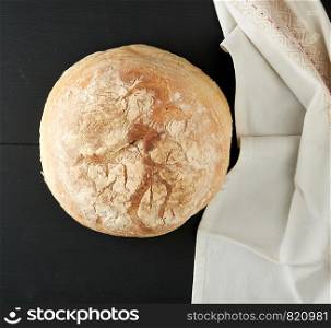 baked round white wheat bread on a textile towel, wooden old table, black background. Homemade food