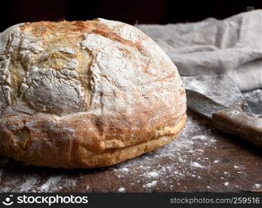 baked round white wheat bread on brown old wooden board, close up