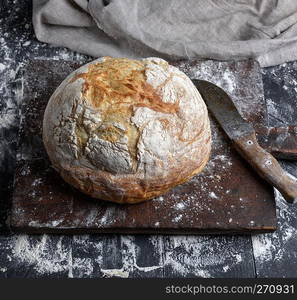 baked round white wheat bread on brown old wooden board, top view