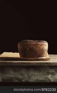 baked rye bread lies flour on a brown paper, wooden old table, black background