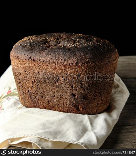 baked rye bread lies flour on a textile towel, wooden old table, black background