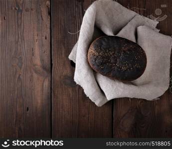 baked rye bread on a gray linen napkin, brown wooden table, top view, copy space