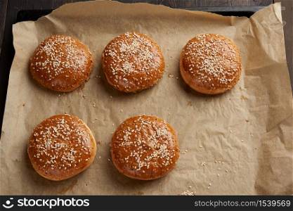 baked sesame buns on brown parchment paper, ingredient for a hamburger, top view