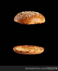 baked sesame seed round bun cut in half, halves fried and levitating in air over each other, black background