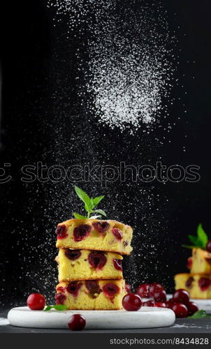 Baked sponge cake with cherries sprinkled with powdered sugar, black background