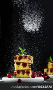 Baked sponge cake with cherries sprinkled with powdered sugar, black background