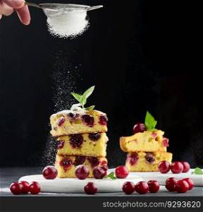 Baked sponge cake with cherries sprinkled with powdered sugar, black background