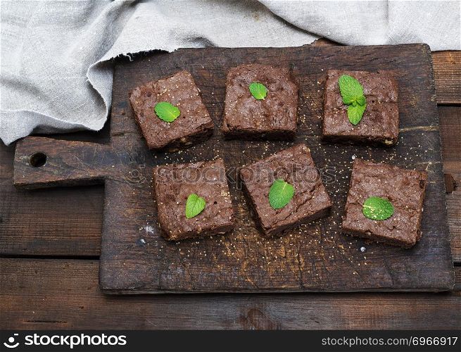 baked square pieces of brownie brownie pie on an old brown wooden cutting board, top view