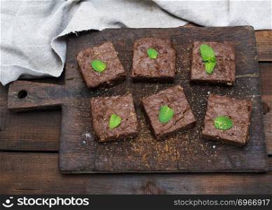 baked square pieces of brownie brownie pie on an old brown wooden cutting board, top view