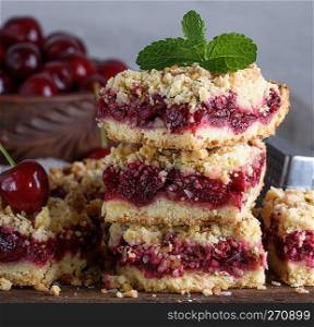 baked square pieces of cake with cherries on a wooden board, crumble cake