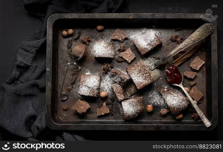 Baked square pieces of chocolate brownie sprinkled with powdered sugar on the table, top view