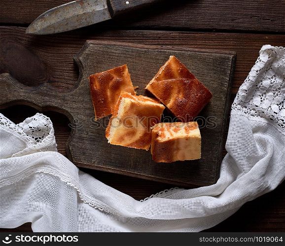 baked square pieces of pumpkin cheesecake on a wooden board, top view on a wooden board, top view