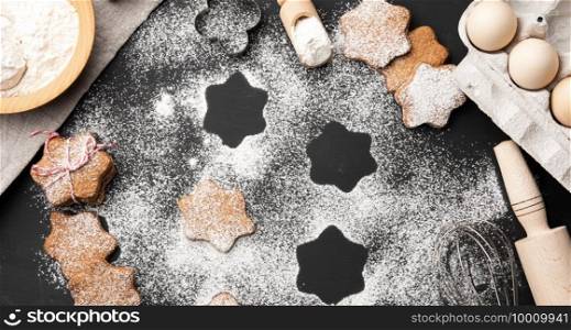 baked star-shaped gingerbread cookie sprinkled with powdered sugar on a black table and ingredients, top view