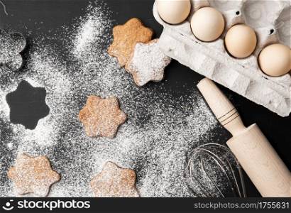 baked star-shaped gingerbread cookie sprinkled with powdered sugar on a black table and ingredients, top view