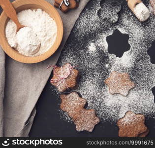 baked star-shaped gingerbread cookie sprinkled with powdered sugar on a black table and ingredients