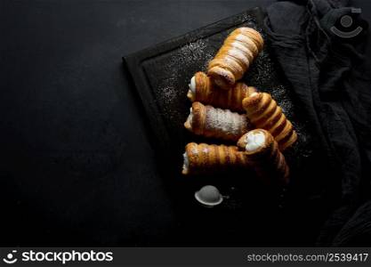 baked tubules filled with whipped egg white cream on a black wooden kitchen board, top view