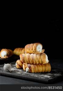 Baked tubules with whipped protein cream on a wooden board, black background