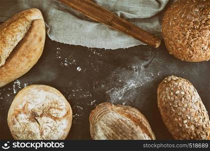 baked various loaves of bread on a black background, empty space in the middle, top view, vintage toning