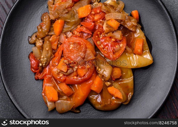 Baked vegetables, eggplant, peppers and carrots on a black plate on a gray concrete background. Vegetarian food. Baked vegetables, eggplant, peppers and carrots on a black plate on concrete background