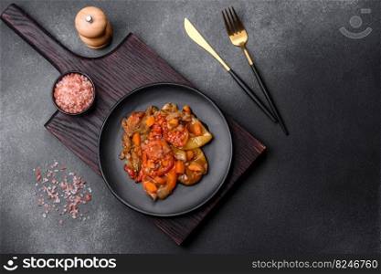 Baked vegetables, eggplant, peppers and carrots on a black plate on a gray concrete background. Vegetarian food. Baked vegetables, eggplant, peppers and carrots on a black plate on concrete background