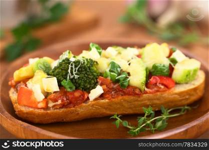 Baked vegetarian open sandwich (red bell pepper, broccoli, zucchini, scallion and cheese on spicy tomato sauce on a bun) on wooden plate (Selective Focus, Focus on the front of the broccoli) . Baked Vegetarian Open Sandwich