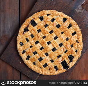 baked whole black currant pie lay on a brown wooden cutting board, top view