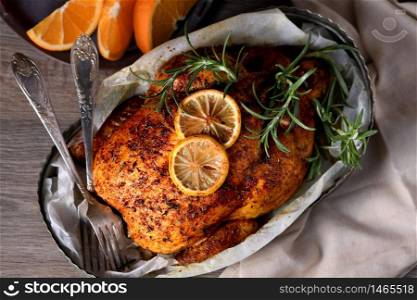 Baked whole chicken in spices with crispy appetizing fried crust in a tray, dark moody
