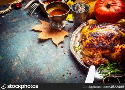 Baked whole chicken or little turkey with sauce, pumpkin and autumn decoration served for Thanksgiving Day on dark rustic wooden background, border, place for text