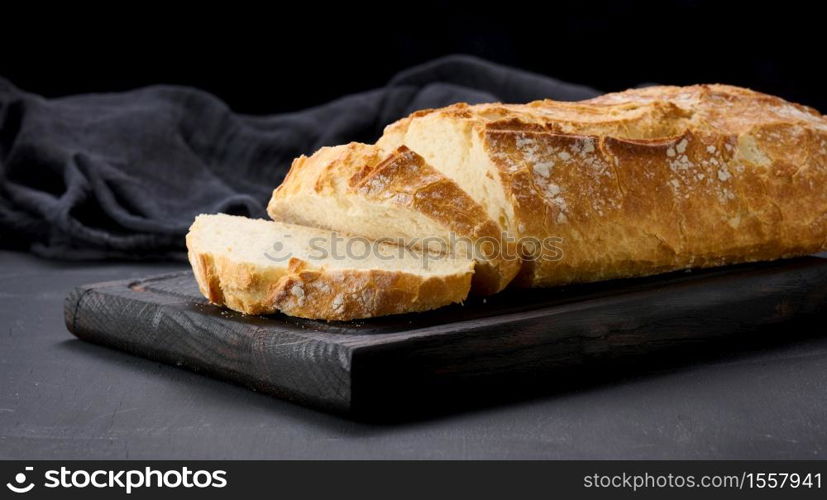 baked whole oval bread made from white wheat flour on a black table, fresh pastries