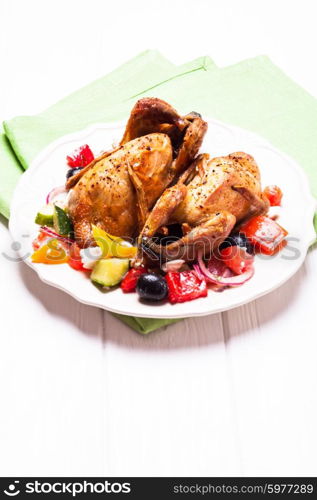 Baked whole quail and fresh vegetable salad in white plate on table with green napkin. Baked quail with salad