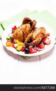 Baked whole quail and fresh vegetable salad in white plate on table with green napkin. Baked quail with salad