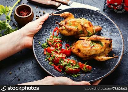 Baked whole quail and vegetable salad.Appetizing baked quail meat on plate in hands. Baked quail and vegetable salad on a plate in hands