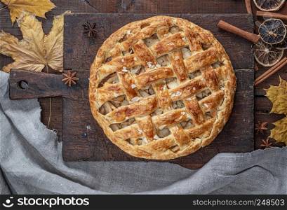 Baked whole round apple pie on a rectangular old brown board, wooden table, top view