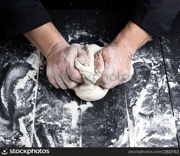 baker kneads white wheat flour dough on a black wooden table, top view