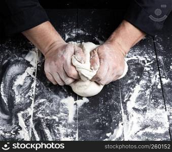 baker kneads white wheat flour dough on a black wooden table, top view
