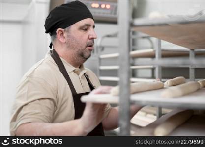 Baker placing tray with formed raw dough on rack trolley ready to bake in the oven. High quality photo. Baker placing tray with formed raw dough on rack trolley ready to bake in the oven