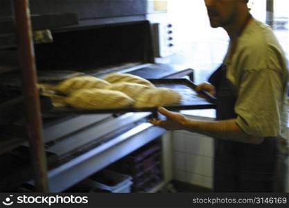 Baker removing bread from oven
