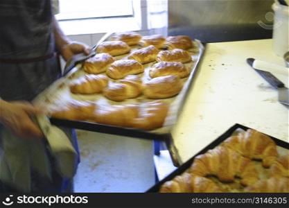 Baker removing croissants from oven