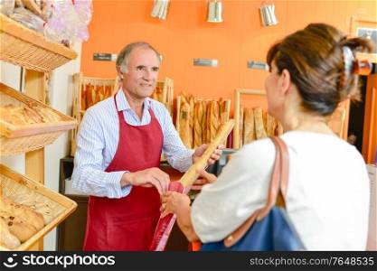 Baker serving a lady with a baguette