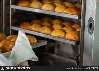 Baker taking baked buns out of the oven in restaurant kitchen . Baker Taking Baked Buns Out Of the Oven
