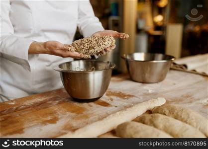 Bakery house concept. Young woman baker making bread or bagels with sesame, poppy, pumpkin and sunflower seeds. Closeup view of hands over metal bowl on table. Baker forming bread or bagels with sesame, poppy, pumpkin and sunflower seeds
