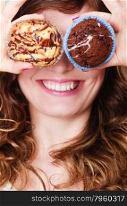 Bakery, sweet food and happiness concept. Closeup smiling woman having fun holding cakes in hands covering eyes with cupcakes