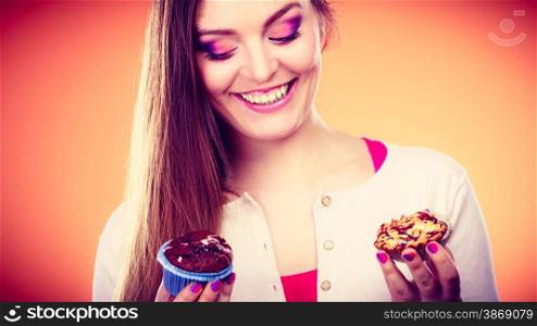 Bakery, sweet food and people concept. Closeup smiling woman holding cakes cupcakes in hands orange background