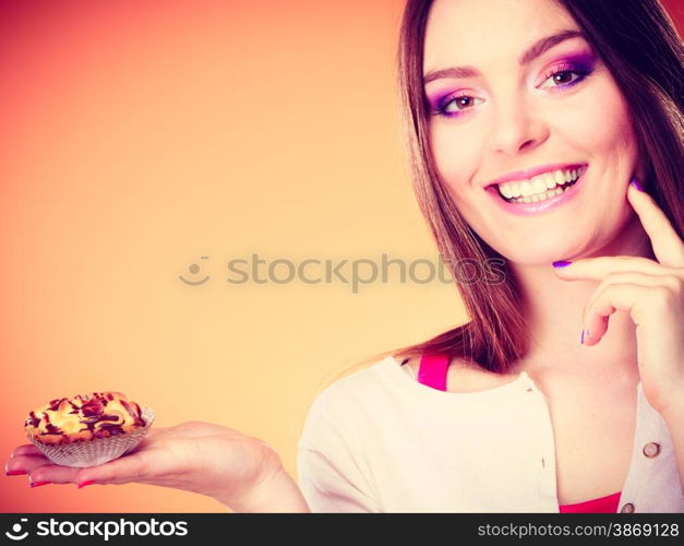 Bakery sweet food and people concept. Smiling woman holds cake cupcake in hand orange background