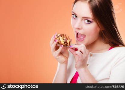 Bakery, sweet food and people concept. Woman wide open mouth holds cake cupcake in hand orange background