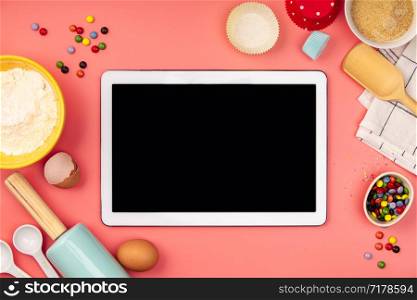 Baking background frame. Ingredients, kitchen items for baking and empty tablet. Kitchen utensils, flour, eggs, sugar. Text space, top view.. Baking ingredients with empty tablet on pink background, flat lay