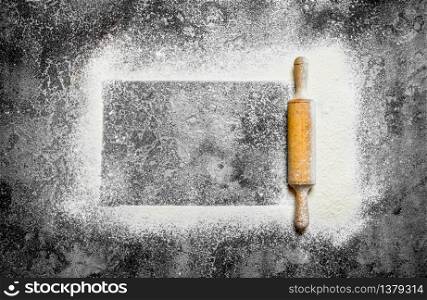 Baking background. Frame of sifted flour with a rolling pin. On rustic background.