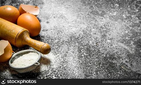 Baking background. Rolling pin with fresh eggs and flour on a rustic background.