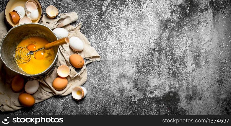 Baking background. Whisking eggs in the old bowl . On rustic background.. Baking background. Whisking eggs in the old bowl .